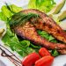 Delicious grilled salmon steak served with avocado, lettuce, cherry tomatoes, and lemon slice on a white plate.